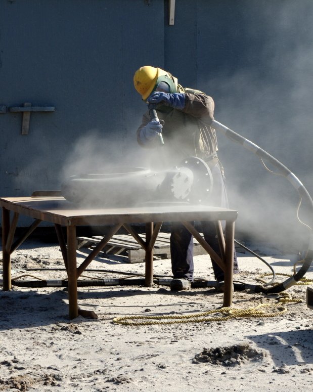 Arbeiter beim Sandstrahlen eines Stahlteils